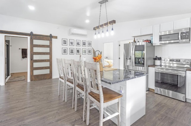 kitchen featuring pendant lighting, stainless steel appliances, a wall mounted AC, a barn door, and white cabinetry