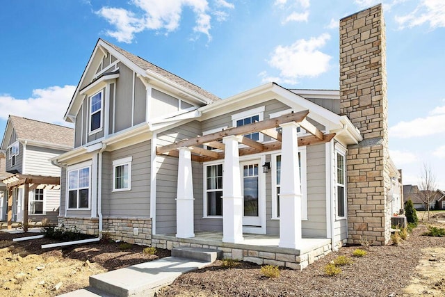 exterior space with covered porch, stone siding, a chimney, and a pergola