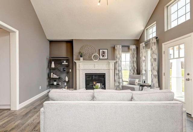 living area featuring a glass covered fireplace, vaulted ceiling, baseboards, and wood finished floors