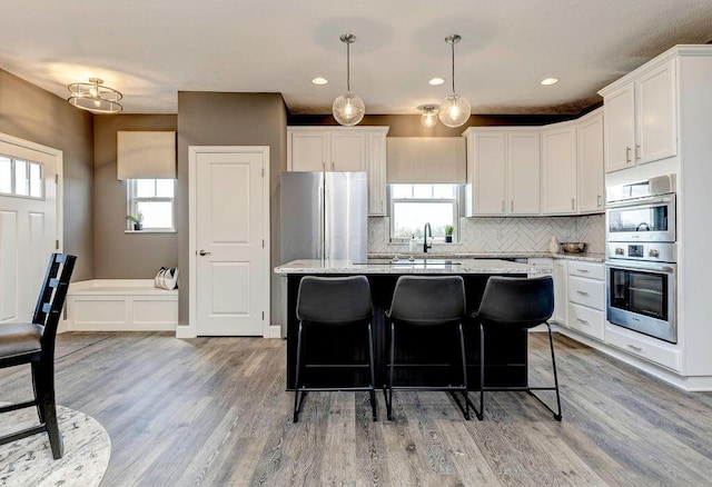 kitchen with a breakfast bar area, light wood-style flooring, a kitchen island, white cabinets, and decorative backsplash