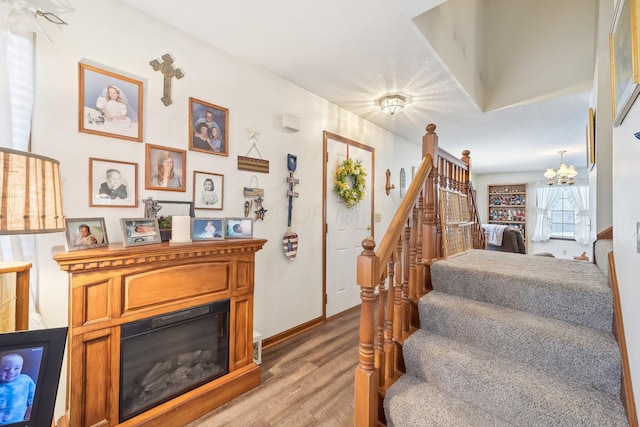 staircase with a chandelier, wood finished floors, and a glass covered fireplace