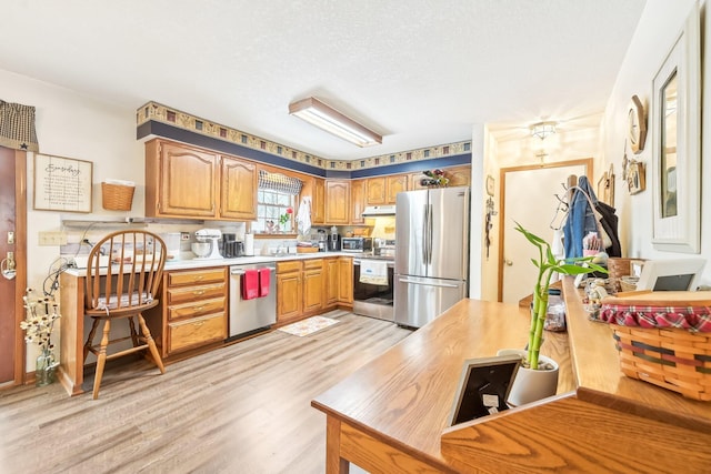 kitchen featuring stainless steel appliances, light countertops, light wood-style flooring, brown cabinetry, and under cabinet range hood