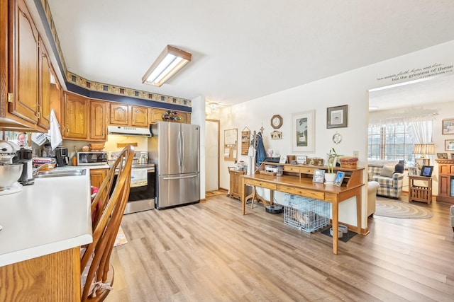 kitchen featuring appliances with stainless steel finishes, brown cabinets, light wood-style flooring, and under cabinet range hood