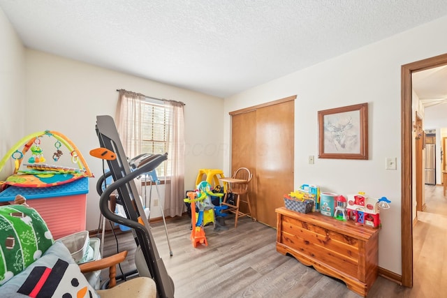 workout area featuring light wood finished floors, baseboards, and a textured ceiling