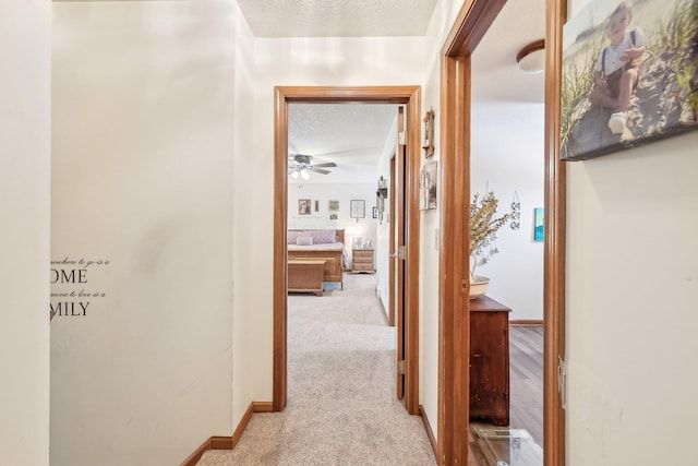 hall with a textured ceiling, carpet flooring, and baseboards