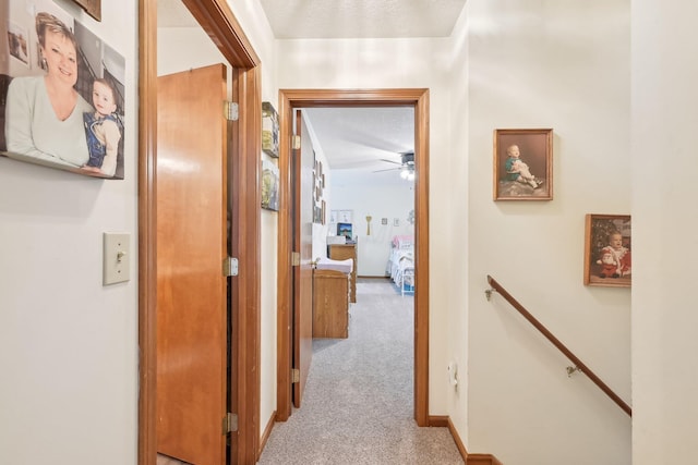 hallway featuring baseboards, carpet flooring, a textured ceiling, and an upstairs landing