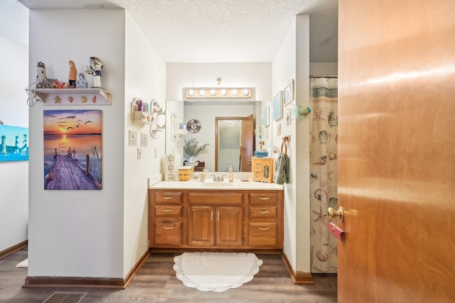 bathroom featuring visible vents, baseboards, wood finished floors, a textured ceiling, and vanity