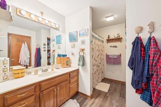 bathroom with a shower with shower curtain, baseboards, wood finished floors, and vanity