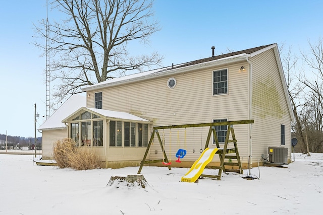 snow covered back of property featuring a playground, a sunroom, and central air condition unit