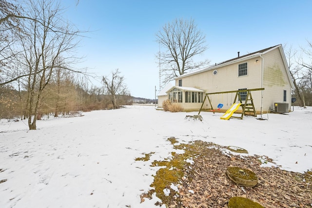 snow covered back of property with a sunroom and central AC unit