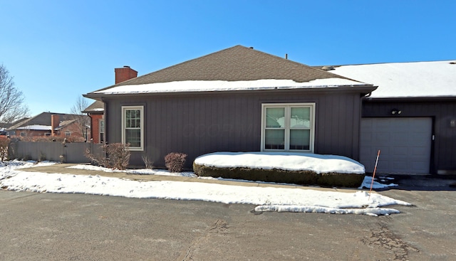 view of front of home with a garage, a shingled roof, a chimney, and fence