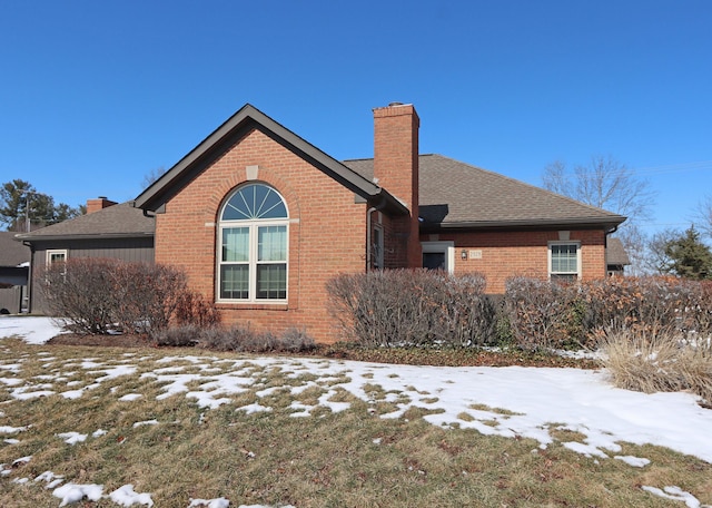 snow covered property with roof with shingles, brick siding, and a chimney