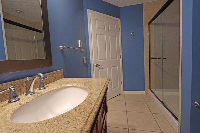 full bath with a stall shower, a textured ceiling, vanity, tile patterned flooring, and baseboards