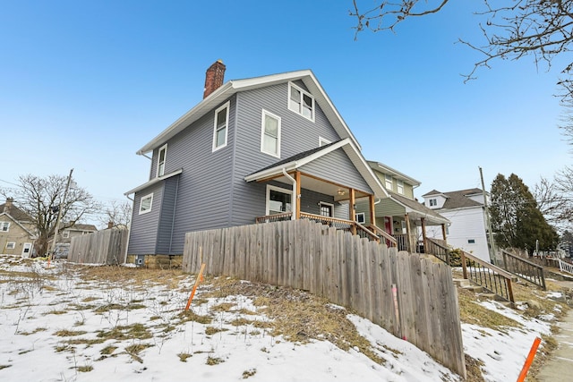 view of front of home featuring covered porch, fence, and a chimney