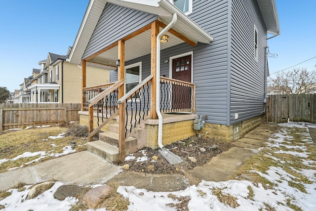 snow covered property entrance featuring covered porch and fence