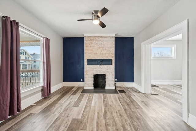 unfurnished living room with a ceiling fan, baseboards, a fireplace, and light wood finished floors