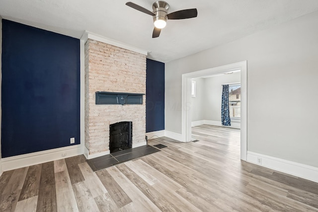 unfurnished living room featuring ceiling fan, baseboards, wood finished floors, and a stone fireplace