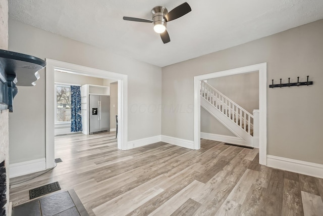 unfurnished room with stairway, visible vents, light wood-style flooring, and baseboards