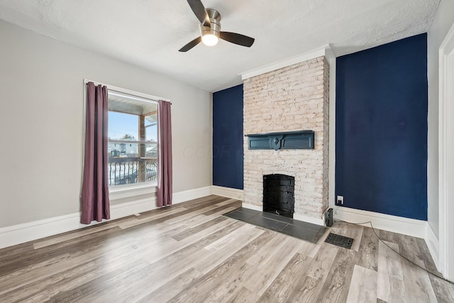 unfurnished living room with light wood-type flooring, baseboards, a textured ceiling, and a stone fireplace