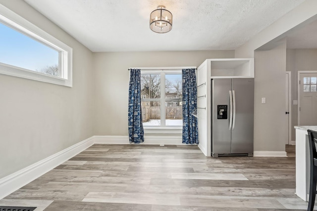 unfurnished dining area with light wood-type flooring, plenty of natural light, and baseboards