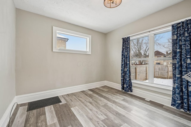 spare room with light wood-type flooring, visible vents, and baseboards