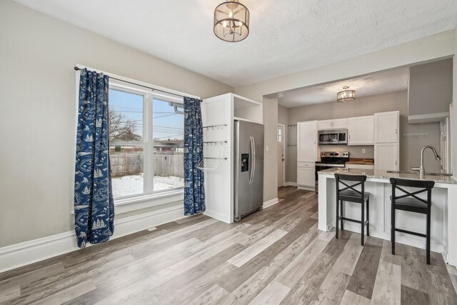 kitchen with a breakfast bar area, a peninsula, white cabinets, appliances with stainless steel finishes, and light wood finished floors