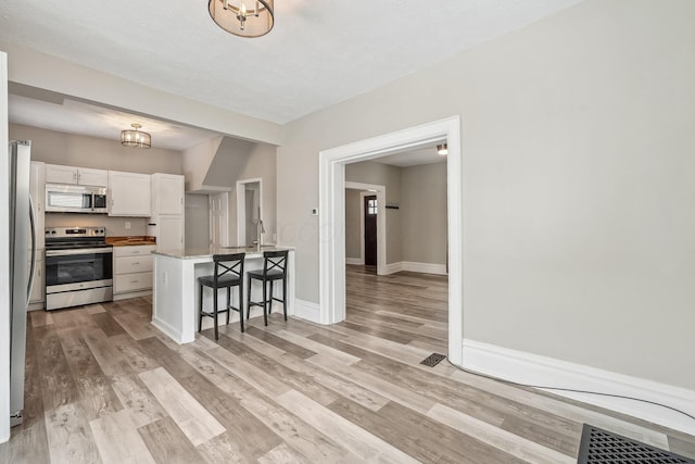 kitchen featuring a kitchen bar, appliances with stainless steel finishes, white cabinetry, light wood-type flooring, and baseboards