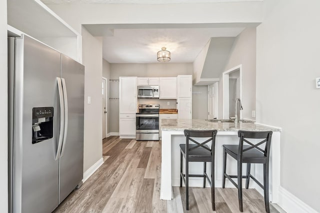 kitchen featuring light stone counters, a breakfast bar area, stainless steel appliances, a sink, and white cabinetry