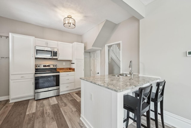 kitchen with a sink, light wood-style floors, white cabinets, appliances with stainless steel finishes, and light stone countertops