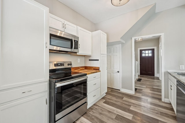 kitchen with baseboards, vaulted ceiling, stainless steel appliances, light wood-type flooring, and white cabinetry