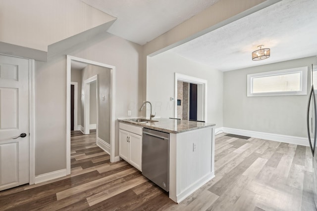 kitchen with light stone counters, a sink, white cabinetry, light wood-style floors, and stainless steel dishwasher