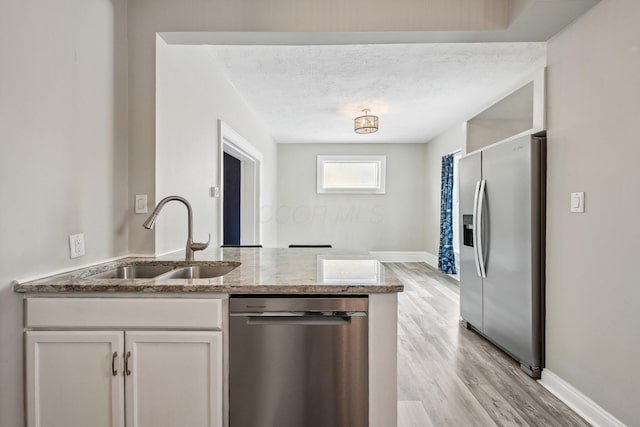 kitchen with a textured ceiling, a sink, white cabinets, appliances with stainless steel finishes, and light wood-type flooring