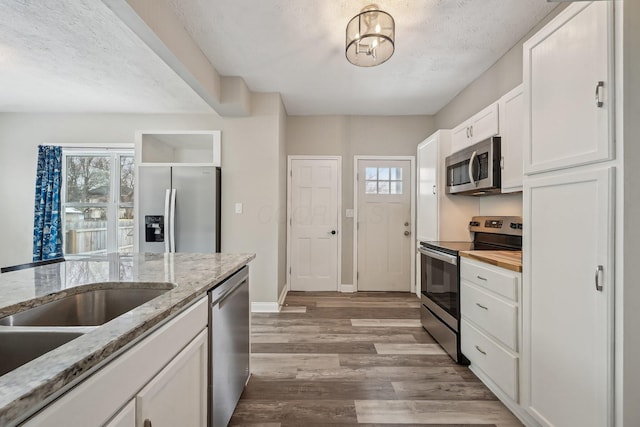 kitchen featuring light wood-style flooring, appliances with stainless steel finishes, white cabinetry, a textured ceiling, and light stone countertops