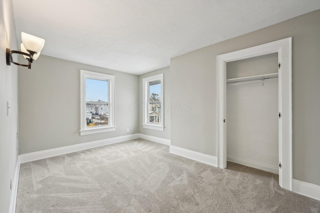 unfurnished bedroom featuring a closet, light colored carpet, a notable chandelier, and baseboards