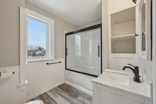 full bath with wood finished floors, wainscoting, vanity, and bath / shower combo with glass door