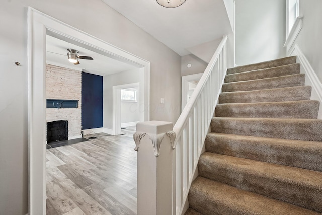 stairs featuring ceiling fan, a fireplace, baseboards, and wood finished floors