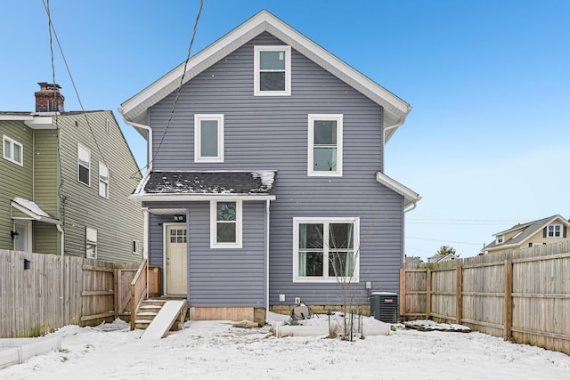 snow covered back of property with entry steps, a fenced backyard, and central AC