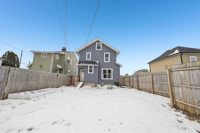 snow covered house featuring a fenced backyard