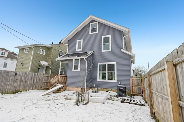 snow covered rear of property with a fenced backyard and central AC unit