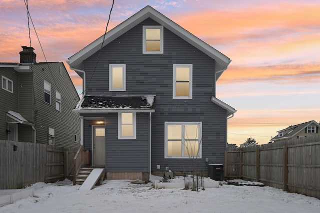 snow covered rear of property with cooling unit, a fenced backyard, and entry steps