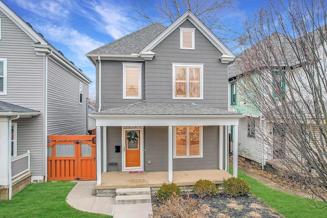 traditional home featuring covered porch, a shingled roof, and a front lawn