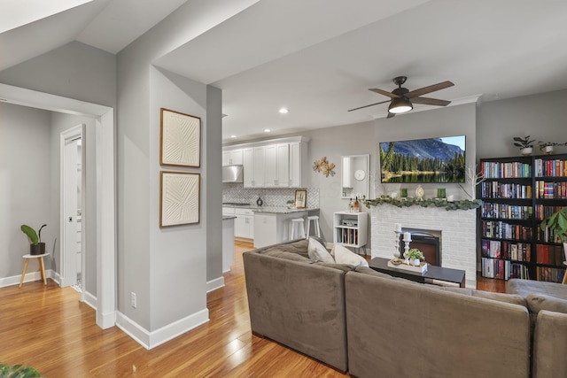 living room with light wood-type flooring, a fireplace, a ceiling fan, and baseboards