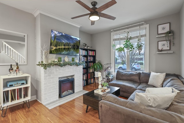 living area featuring ceiling fan, a fireplace, wood finished floors, baseboards, and ornamental molding