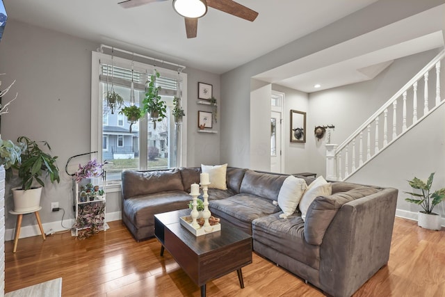 living area with light wood-style flooring, stairs, baseboards, and a ceiling fan