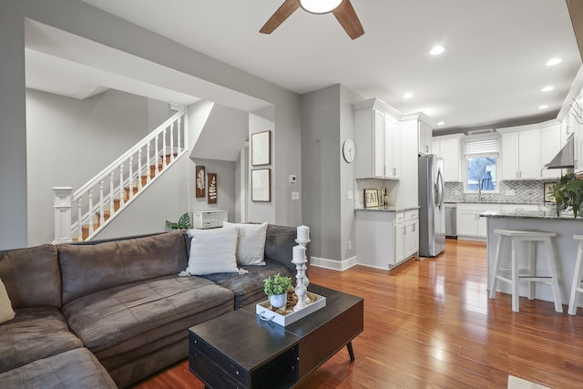 living room featuring light wood finished floors, recessed lighting, ceiling fan, baseboards, and stairs