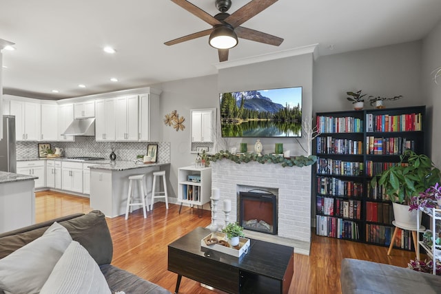 living area with a brick fireplace, light wood finished floors, a ceiling fan, and recessed lighting