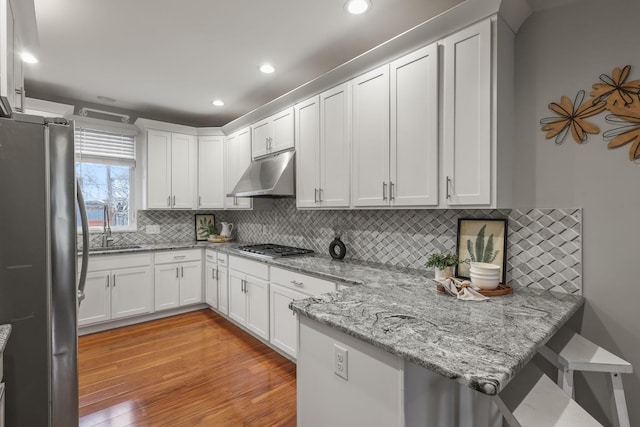 kitchen with stainless steel appliances, light wood-style flooring, a sink, a peninsula, and under cabinet range hood