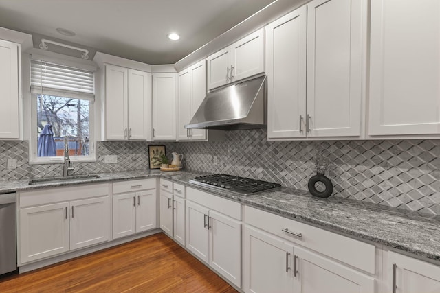 kitchen with light wood-style floors, appliances with stainless steel finishes, under cabinet range hood, white cabinetry, and a sink