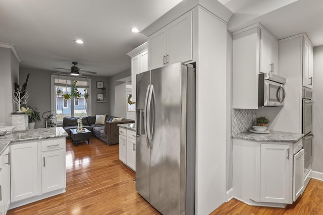 kitchen with open floor plan, appliances with stainless steel finishes, light wood finished floors, and white cabinets