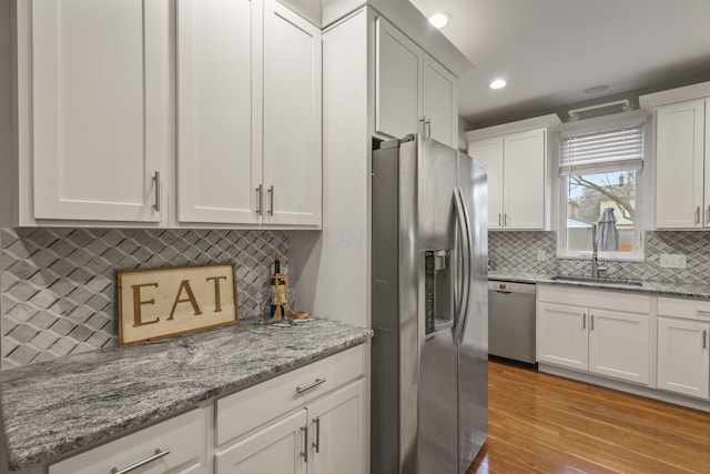 kitchen featuring tasteful backsplash, appliances with stainless steel finishes, light stone countertops, light wood-style floors, and white cabinetry